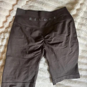 Bruna träningstights-shorts från Relode - Snygga bruna shorts från Relode med hög midja och scrunch-detalj bak. De är tillverkade i mjukt och stretchigt material som passar perfekt för gymmet eller andra sportaktiviteter. Modellen är tight och har en ribbad linning för extra komfort. (‼️dem har ett mini hål men eftersom jag alltid viker ner dom då de är så höga så synd de aldrig)‼️dom är även lite noppriga 