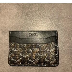 Goy4rd plånbok i svart och brunt - Snygg och smidig plånbok från Goy4rd med klassiskt mönster i svart, brunt och vitt. Tillverkad i skinn med flera kortfack och diskret logga framtill. Perfekt för dig som vill ha något stilrent och exklusivt i fickan.