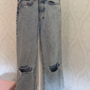 Ljusblå wide jeans med slitningar - Säljer ett par ljusblå jeans med bred passform och rejält slitna knän. Jeansen har regular waist och är i klassisk denim med snygg tvätt. Perfekta för dig som gillar en avslappnad och trendig stil.