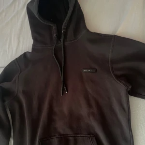 Svart hoodie från Aspact med huva - Svart hoodie från Aspact med stilren logga på bröstet. Klassisk modell med huva och snörning samt känguruficka framtill. Storlek L men passar M också.