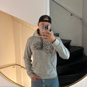 Grå hoodie från Polo Ralph Lauren - Säljer en grå hoodie från Polo Ralph Lauren med svart logga framtill. Klassisk modell med huva, känguruficka och svarta snören. Mjuk och skön i bomullsmix, perfekt för chill dagar eller när du vill ha en clean streetstyle.