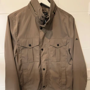 Beige jacka från J.Lindeberg - Snygg beige jacka från J.Lindeberg med stilrena detaljer. Jackan har långa ärmar och knappar framtill samt två bröstfickor med lock. Perfekt för en stilren look. Org pris är 3400 kr, bara att skriva vid fler funderingar