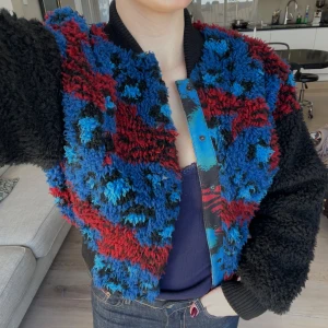 Kenzo x H&M bomberjacka - Säljer en unik och färgglad teddyjacka från Kenzo x H&M. Jackan har ett mönster i blått, rött och svart med en stor broderad tiger och texten 'Jungle Kenzo Paris' på ryggen. Den har långa ärmar och stängs med knappar framtill😊