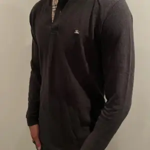 Snygg svart långärmad pikétröja från Burberry med klassisk krage och knappslå. Tröjan har ett diskret logotypbroderi på bröstet och en stilren design med rutigt mönster på insidan av kragen. Perfekt för en stilren look.  