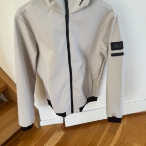Beige jacka från Jack & Jones - Snygg beige jacka från Jack & Jones med huva och dragkedja. Jackan har svarta detaljer och en patch på ärmen. Passar perfekt som vårjacka. Perfekt för en stilren look. Väldigt bra skick, använd fåtal gånger. Storlek:S. Nypris: 699kr. Säljer för 399kr. Pris kan diskuteras