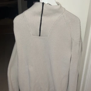 Vit stickad tröja med dragkedja Tom Tailor - Säljer en stilren beige stickad tröja med en unik dragkedja i ryggen. Tröjan har en hög krage och långa ärmar, perfekt för kyligare dagar. Passar både till jeans och kjol! Köpt från tom tailor och använt fåtal gånger