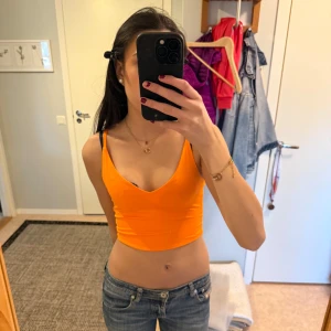 Orange croppad linnetopp - Säljer en snygg orange croppad linnetopp med smala axelband. Perfekt för sommardagar och att matcha med jeans eller kjol. Toppen har en enkel och stilren design.