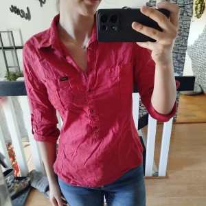 Röd skjorta med knappar - Storlek L men passar även som M.  Snygg röd skjorta med knappar och bröstficka. Perfekt för en avslappnad stil. Ärmarna kan rullas upp för en mer casual look.