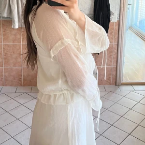 Vit klänning med volangdetaljer - Säljer en söt vit klänning med volangdetaljer och långa ärmar. Klänningen har en luftig passform och knytband vid ärmsluten. Perfekt för en somrig look!