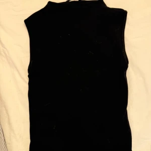 Svart ärmlös väst - Snygg svart ärmlös  topp i ett stilrent och enkelt snitt. Perfekt för att lägga till en extra touch till din outfit. Passar bra till både vardag och speciella tillfällen.