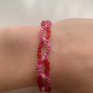 armband i rött och rosa - Unikt armband med små pärlor i rött och rosa. Armbandet har en flätad design som ger en lekfull och färgglad look. Perfekt för att lägga till en pop av färg till din outfit! Kostar bara 15kr!