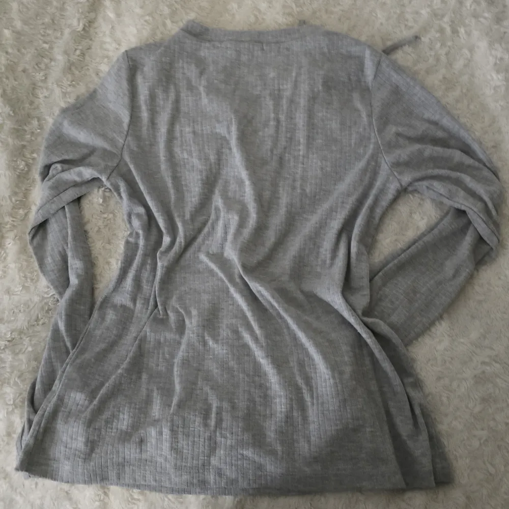 Säljer en stilren grå långärmad tröja från BikBok med snörning framtill. Perfekt för en avslappnad look. Tröjan har en mjuk och bekväm passform. Det står att storleken är M men är som s men jag har storlek xs och använde den. Neuletakit & Villapaidat.
