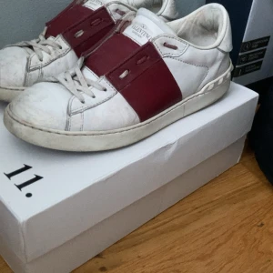 Valentino Open sneakers i vitt och vinrött - Snygga Valentino Open sneakers i vitt med vinröda detaljer. Skorna har en stilren design med breda band över snörningen och en bekväm sula. Perfekta för en trendig look.