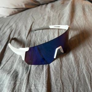 Sportiga solglasögon med blått visir - Snygga sportglasögon med ett futuristiskt blått visir och vit båge. Perfekta för utomhusaktiviteter med en modern och stilren design.