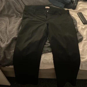 Svarta kostymbyxor från Nelly - Snygga svarta kostymbyxor från Nelly med en klassisk design. Byxorna har en rak passform och är perfekta för en stilren look. De har hällor för bälte och en diskret bakficka.