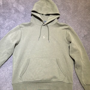 Grön hoodie från Polo Ralph Lauren - Säljer en stilren grön hoodie från Polo Ralph Lauren. Den har en klassisk design med en liten logotyp på bröstet och en praktisk magficka. Perfekt för en avslappnad look. Är lite liten i storlek.