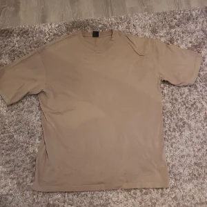 Beige t-shirt från Bershka - Säljer en beige t-shirt från Bershka i oversize passform. Perfekt för en avslappnad stil. Tillverkad i ett mjukt material som känns skönt mot huden.