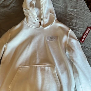 Vit hoodie från Alpha Industries - Säljer en stilren vit hoodie från Alpha Industries med stor logga på ryggen och en klassisk Remove Before Flight-tag. Pris kan diskuteras självklart🙌 Bara att ställa frågor om det är något ni undrar😄