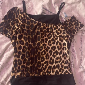 Leopardmönstrad offshoulder topp - Trendig leopardmönstrad topp med offshoulder-design och smala axelband. Perfekt för en djärv look.