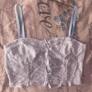 Ljusblå spetstopp med rosetter - Säljer en söt ljusblå topp med spetsdetaljer . Den har flera rosetter framtill som ger en romantisk touch. Perfekt för att piffa upp vilken outfit som helst!aldrig används, kommer tyvärr inte ihåg vart den är köpt ifrån