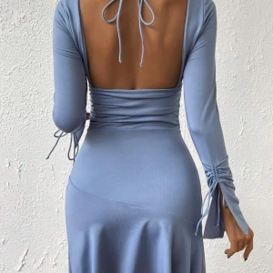 Ljusblå klänning med öppen rygg - Snygg ljusblå klänning med långärmad design och v-ringning. Klänningen har en öppen rygg och knytband vid ärmarna för extra stil. Perfekt för en elegant look. Säljer för att storleken passade mig inte.