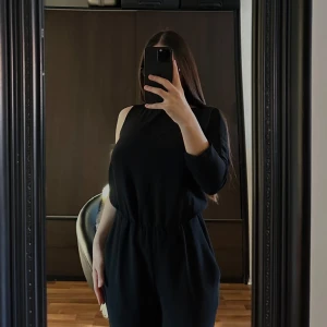Jumpsuit  - Snygg svart jumpsuit från Zara med en elegant design. Den har en lång ärm och en axelbandslös stil på ena sidan, vilket ger en unik look. Perfekt för en stilren och modern outfit. Dragkedja i ryggen för enkel påklädning.🥰🥰🥰