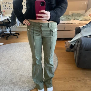 Olivgröna byxor med knappar - Snygga olivgröna byxor med bootcut-stil. Byxorna har dekorativa knappar och fickor framtill, vilket ger en cool look. Perfekta för en avslappnad stil.