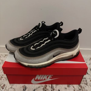 Nike Air Max 97 - Säljer ett par stilrena Nike Air Max 97 i svart och grå. Skorna har en ikonisk vågig design med synlig Air-dämpning i sulan för extra komfort. Perfekta för alla lägen. 