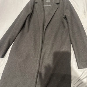 Svart kappa från Zara - Elegant svart kappa från Zara med klassisk design. Perfekt för kyligare dagar med sin stilrena look och långa ärmar. Tillverkad i ett mjukt material som ger en bekväm passform. 