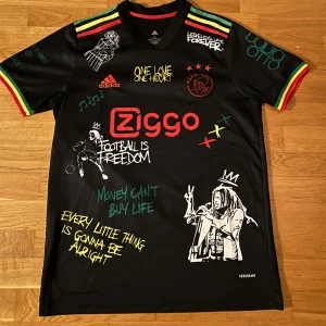 Svart fotbollströja med Ajax x Bob Marley - Säljer en unik svart Ajax fotbollströja från Adidas med Bob Marley-tema. Tröjan har färgglada detaljer i rött, gult och grönt samt tryck med Bob Marley och inspirerande citat. Perfekt för fans av både fotboll och reggae. Passar både M och L