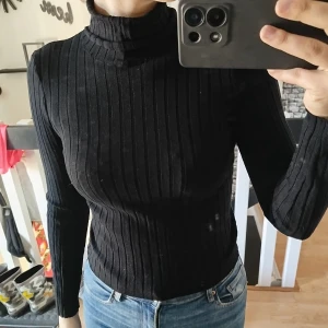 Svart ribbad polotröja - Snygg svart ribbad polotröja med långa ärmar. Perfekt för en stilren look och passar bra till jeans eller kjol. Tröjan har en tight passform som framhäver figuren.