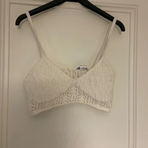 Vit stickad topp från Zara - Säljer en söt vit stickad topp från Zara med smala axelband. Perfekt för varma dagar eller som ett lager under en jacka. Toppen har ett fint mönster och är både stilren och bekväm.