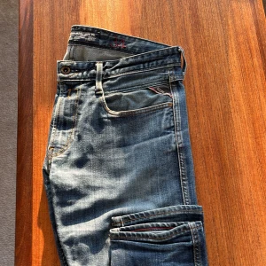 Blå jeans från Replay - Snygga blå jeans från Replay med klassisk femficksdesign och subtila slitningar. Jeansen har en normal passform och är perfekta för en avslappnad stil. Märkesdetaljer syns på bakfickan och linningen. 34-32