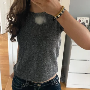 Glittrig topp i silver/guld - Säljer en snygg glittrig topp i silver med korta ärmar. Perfekt för att lysa upp vilken outfit som helst. Toppen har en tight passform och är tillverkad i ett syntetmaterial som ger en skimrande effekt. Passar bra till både jeans och kjol. Storlek 158/164 men passar mig som bär Xs/S, bilderna är mina egna! Använd ca 2 gånger. Pris kan diskuteras 