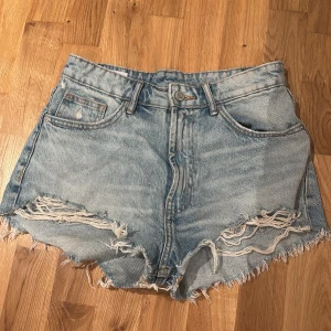Högmidjade jeansshorts från Zara - Snygga ljusblå jeansshorts från Zara med hög midja och råa, slitna kanter. Klassisk femficksmodell med dragkedja och knapp framtill. Perfekta för sommaren!