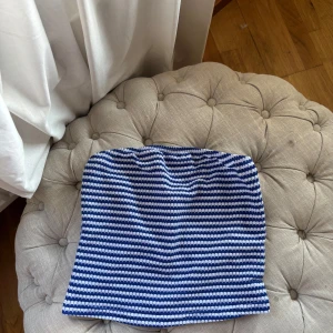 Randig blåvit tubtopp - Säljer en tubtopp med blå och vita ränder. Toppen är bandeau-modell och har en enkel, rak passform. Perfekt för varma dagar och enkel att styla med jeans eller kjol.