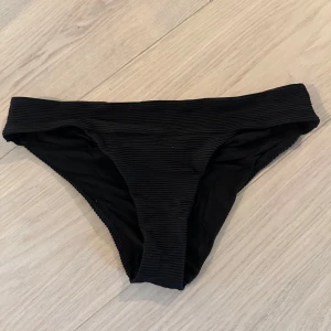 Svarta ribbade bikinitrosor - Snygga svarta bikinitrosor med ribbad struktur och klassisk passform. Perfekta för stranden eller poolen, med en stilren look som passar till det mesta. Materialet känns mjukt och följsamt mot huden.