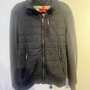 Svart fleecejacka Parajumpers S - Svart cardigan från Parajumpers med dragkedja framtill, tre fickor med dragkedja och snyggt broderat PJS-märke på ärmen. Jackan har ribbade muddar och en sportig look, perfekt för dig som gillar stilren och funktionell design.