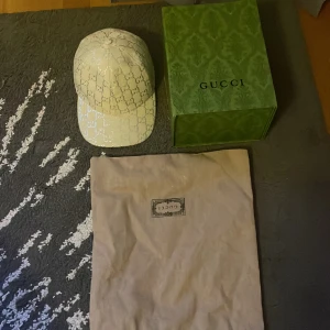 Gucci vit box och allt med - Exklusiv vit keps från Gucci med glittrigt GG-mönster över hela kepsen. Klassisk böjd skärm och justerbar rem bak. Kepsen kommer med originalkartong och dustbag. Perfekt för dig som vill sticka ut med en lyxig accessoar.