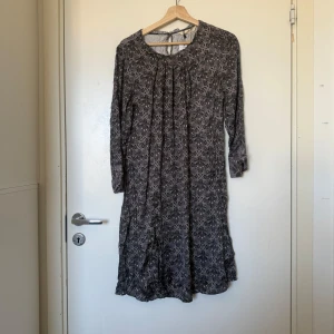 Mönstrad grå klänning med trekvartsärm - Grå klänning med mörkgrått och vitt mönster, rund halsringning och trekvartsärmar. Lätt och flowy modell med knytning i nacken och diskret rynk vid axlarna. Perfekt för dig som gillar en avslappnad men ändå snygg stil.Från märket Odd Molly i storlek 2 som enligt deras storleksguide motsvarar en storlek M. Helt ny med tags. 