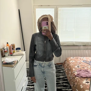 Grå skinnjacka från Fashion Nova - Säljer en grå skinnjacka från Fashion Nova med rak passform och cool ståkrage. Jackan har dragkedja framtill och är croppad i modellen. Perfekt för dig som vill ha en stilren och edgy look till vardags. Långärmad och i syntetmaterial.
