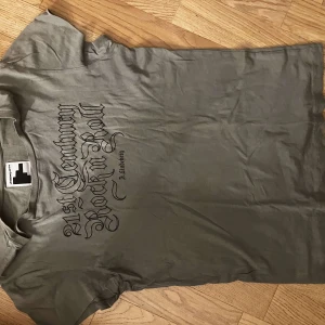 Grå t-shirt J.Lindeberg  - Snygg grå t-shirt från J.Lindeberg med svart tryck på bröstet där det står '21st Century Rock n Roll'. Klassisk passform med rund hals och korta ärmar. 🩷