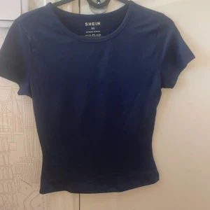Mörkblå topp från SHEIN XS - Enkel och stilren mörkblå topp från SHEIN i storlek XS. Modellen är figurnära med rund halsringning och korta ärmar. Perfekt att matcha med jeans eller kjol för en clean look.