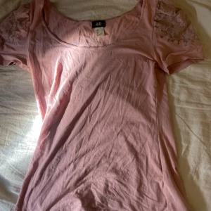Rosa blus med spetsärmar från H&M - Bra skick!! Söt ljusrosa blus från H&M med korta ärmar och spetsdetaljer på axlarna. Blusen har en rundad halsringning och är gjord i mjuk bomull, perfekt för en chill och feminin look.