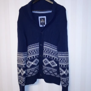 Mörkblå kofta från Hampton Republic - Snygg mörkblå kofta från Hampton Republic med klassiskt vitt mönster. Koftan är stickad, har långa ärmar, knappar framtill och två fickor. Perfekt för kalla dagar och ger en chill, stilren vibe. Kan skickas med extra pris via post.