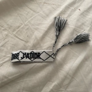 Christian Dior broderat armband - Snyggt svart vit armband från Christian Dior J'Adior'. Armbandet är gjort i ett flätat tygmaterial. Pris kan diskuteras i dm