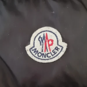 Svart dunväst från Moncler XXL passar även L-XL - Snygg svart dunväst från Moncler med quiltad design och huva. Västen har två stora dragkedjefickor framtill, tydlig Moncler-logga på bröstet och dragkedja hela vägen. Perfekt för lager-på-lager och streetstyle. Enda defekter syns på bild 4. "haken" på dragkedjan har lossnat men den fungerar endå. Säljes endast för jag minskat i vikt. Pris ej ristat i sten. 