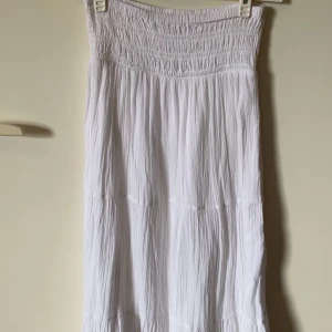 Vit långklänning från Gina Tricot - Luftig vit långklänning från Gina Tricot med smock upptill och böljande tyg. Klänningen har en enkel och stilren design, perfekt för varma dagar. Tillverkad i mjuk bomull som känns skön mot huden.