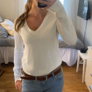 Vit v-ringad långärmad tröja - Säljer en stilren vit långärmad tröja med v-ringning. Tröjan har en enkel och clean design som passar perfekt till jeans eller kjol. Mjuk och skön att bära, perfekt för lager-på-lager under kyligare dagar.