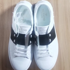 Valentino Garavani Open sneakers vit/svart - Snygga Valentino Garavani Open sneakers i vitt skinn med bred svart läderdetalj över vristen. Klassisk rund tå, vita snören och coola nitar på hälen. Perfekta för dig som vill ha en stilren men ändå unik look.